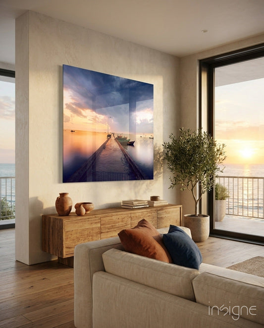 Framed glass artwork depicting a wooden jetty at sunset with boats, displayed above wooden dresser in modern coastal living room.