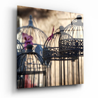 Three decorative black birdcages with purple flowers casting geometric shadows on beige wall background.