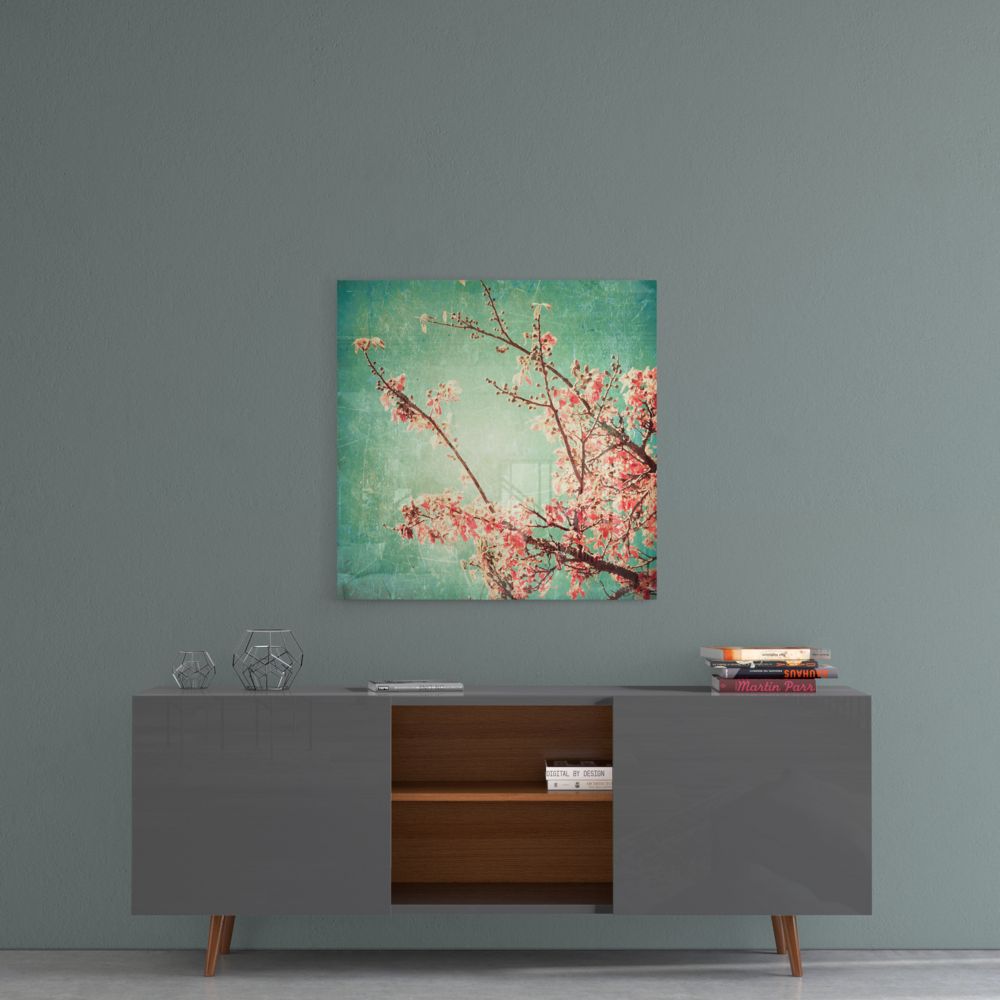 Square glass wall art with pink cherry blossoms and branches on turquoise-green gradient background, hung above mid-century modern sideboard.