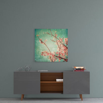 Square glass wall art with pink cherry blossoms and branches on turquoise-green gradient background, hung above mid-century modern sideboard.