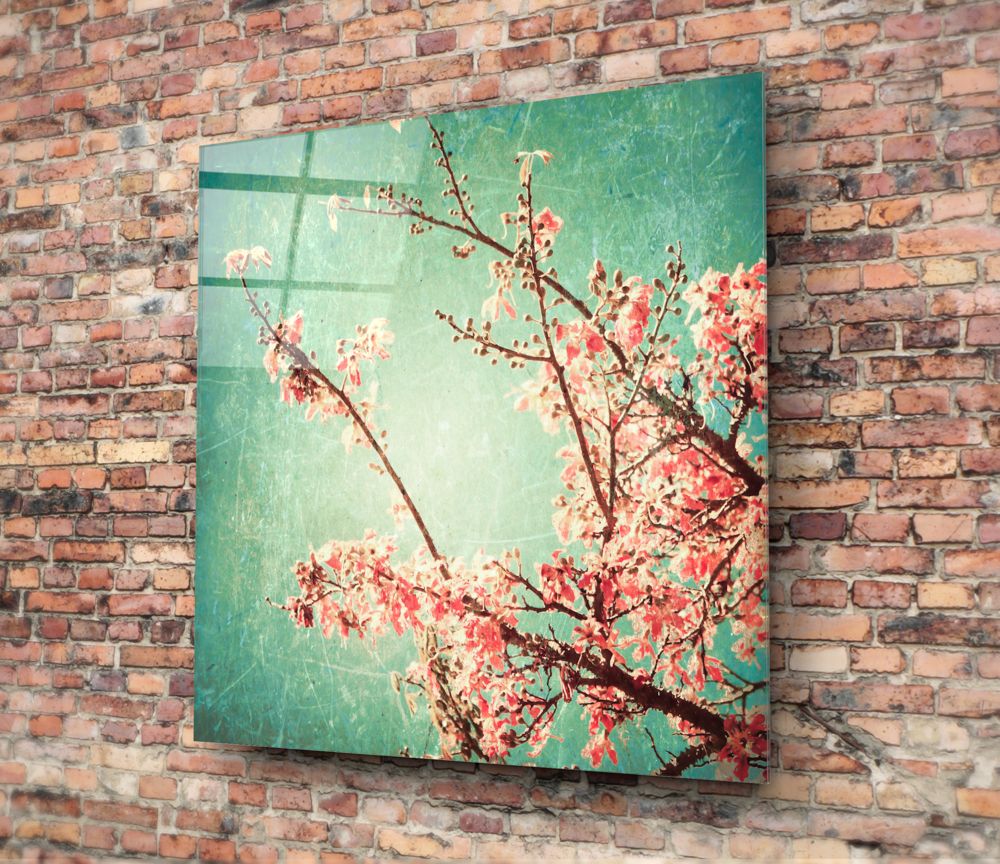 Cherry blossom glass wall art mounted on brick wall, showing turquoise background with red and pink flowering branches.