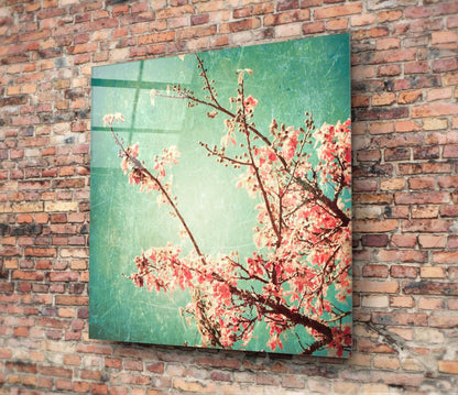 Cherry blossom glass wall art mounted on brick wall, showing turquoise background with red and pink flowering branches.