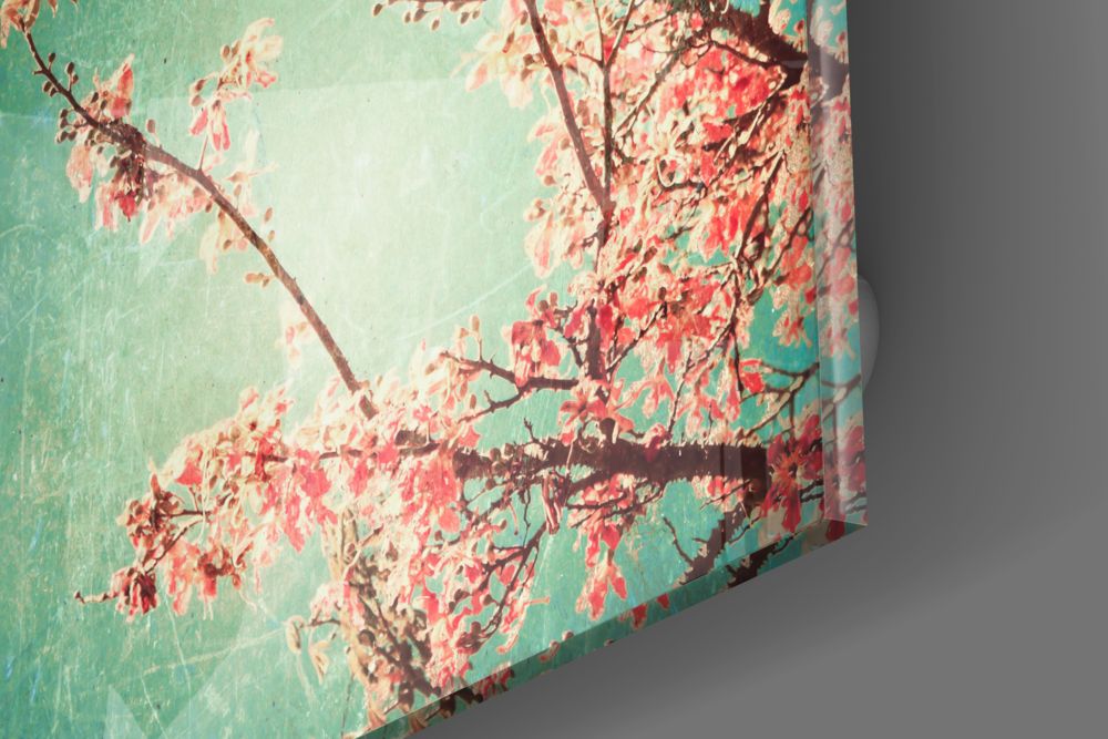 Cherry blossom glass wall art showing red blossoms and branches against turquoise background, angled three-quarter view.