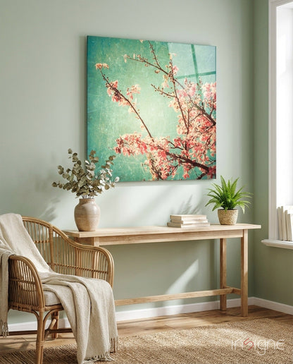 Cherry blossom glass wall art in turquoise and pink tones displayed above a wooden desk in a sunlit room.