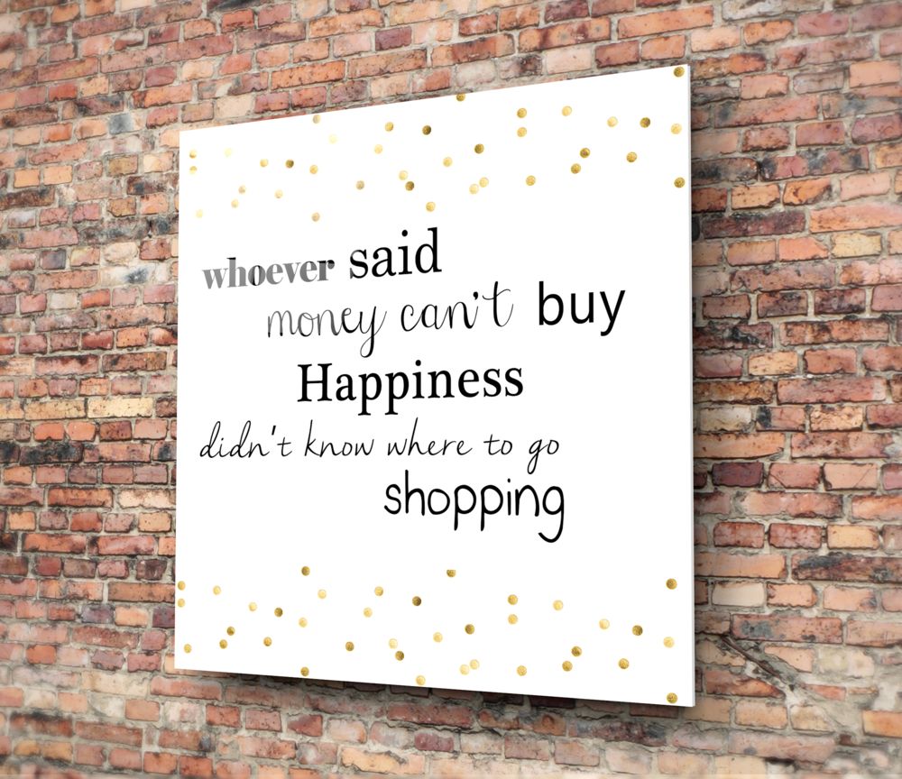 White glass wall art with gold polka dots mounted on brick wall, featuring humorous shopping quote in mixed typography.