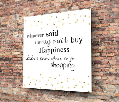 White glass wall art with gold polka dots mounted on brick wall, featuring humorous shopping quote in mixed typography.