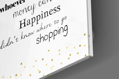 Close-up angled view of white glass wall art with black handwritten text and gold foil dots, displaying shopping-related phrases.