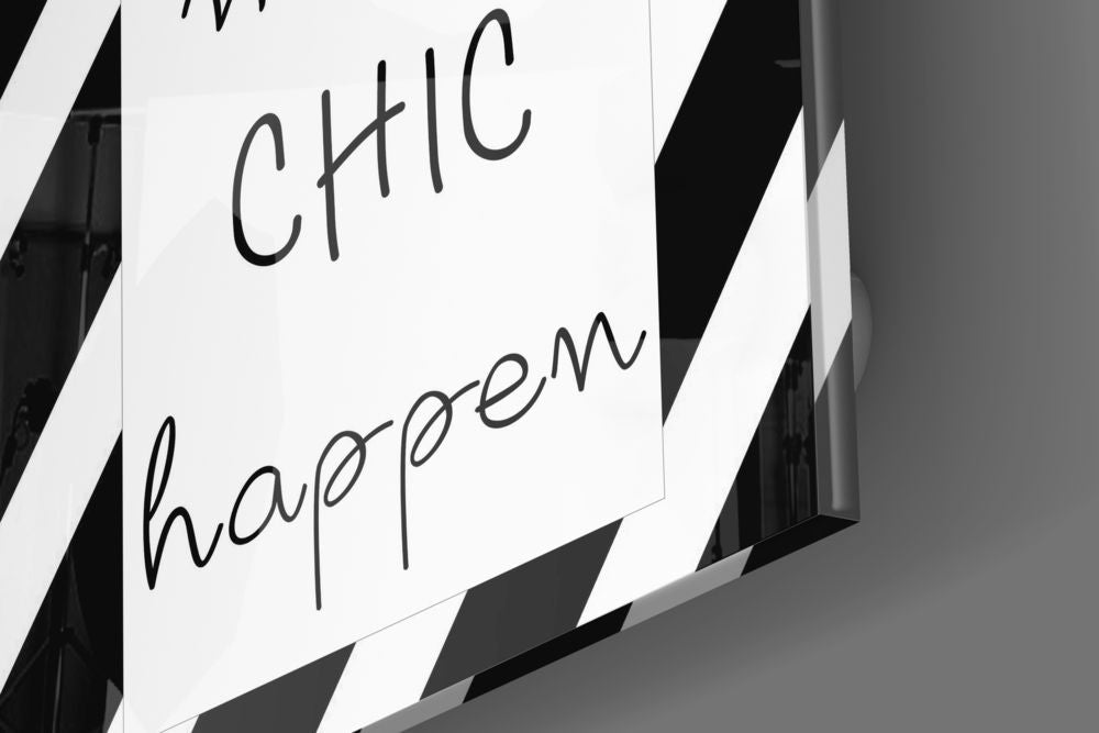 Close-up of white glass wall art with handwritten-style black text reading "CHIC" and "happen," photographed at an angle against a dark background.