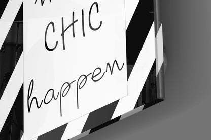 Close-up of white glass wall art with handwritten-style black text reading "CHIC" and "happen," photographed at an angle against a dark background.