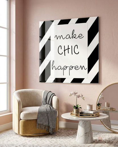 Black and white striped glass wall art with "make CHIC happen" text displayed above cream armchair in styled living room.