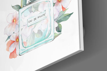 Angled view of glass wall art featuring a turquoise perfume bottle with "Eau De Toilette" label surrounded by watercolor pink and coral flowers with green leaves.