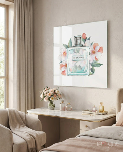 Framed watercolor artwork depicting a clear glass perfume bottle labeled "Eau De Toilette" surrounded by pink and white flowers with green leaves, displayed above a marble vanity desk in a bedroom.