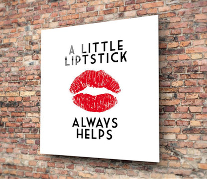 White glass wall art with red lip print and gray and black text reading "A LITTLE LIPSTICK ALWAYS HELPS" mounted on exposed brick wall.