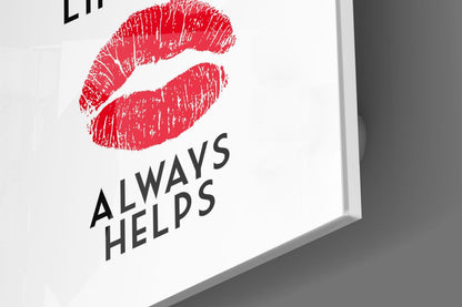 Close-up angled view of white glass wall art featuring a red lipstick print and black text reading "ALWAYS HELPS.