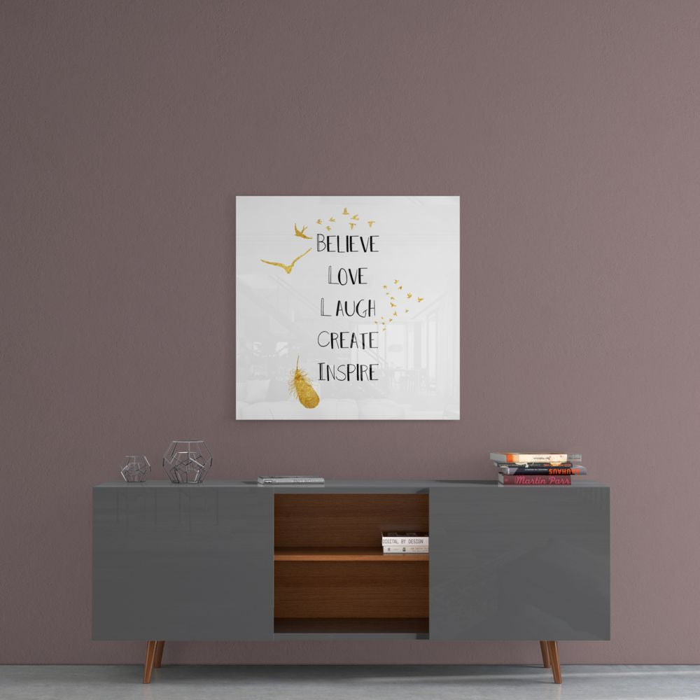 Square glass wall art with gold flying birds and text reading "Believe Love Laugh Create Inspire" displayed above a gray mid-century modern sideboard.