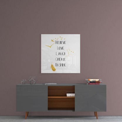 Square glass wall art with gold flying birds and text reading "Believe Love Laugh Create Inspire" displayed above a gray mid-century modern sideboard.