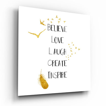 White glass wall art with gold foil birds and inspirational text reading "Believe Love Laugh Create Inspire" displayed at an angle.