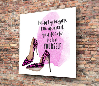 Glass wall art with pink watercolor background, magenta leopard print heels, and black motivational text mounted on brick wall.
