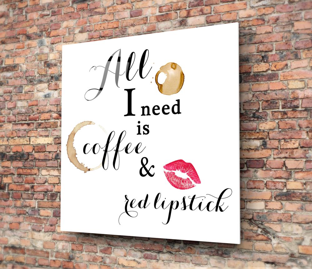 White glass wall art with black cursive text reading "All I need is coffee & red lipstick," decorated with coffee stain and lipstick mark illustrations, mounted on brick wall.