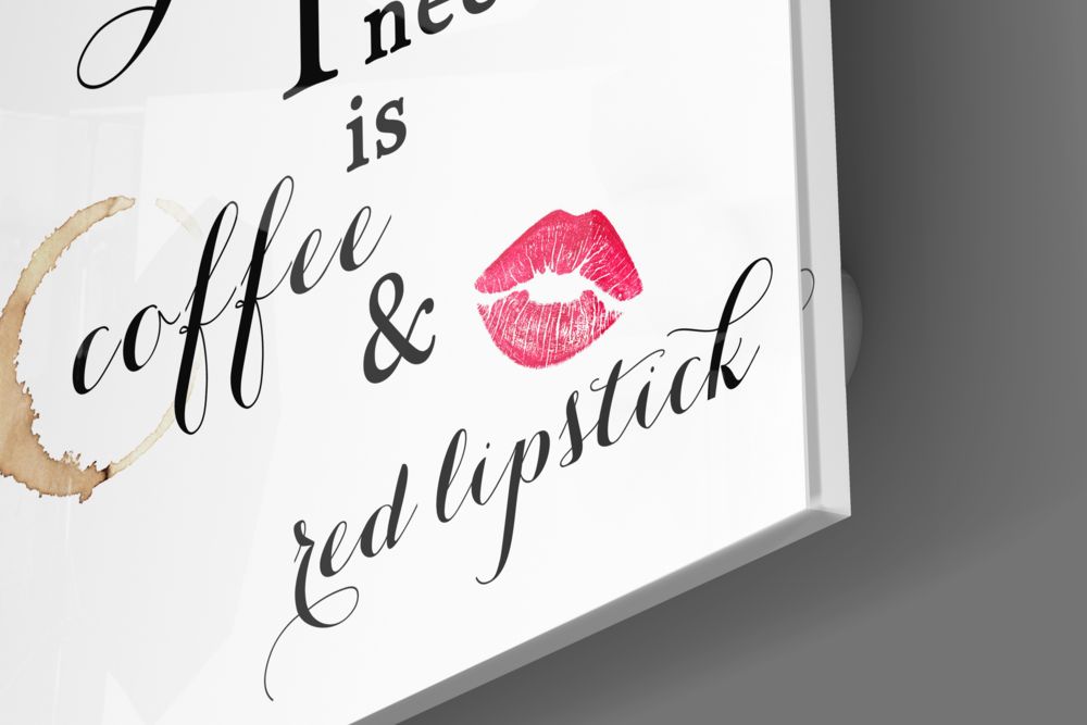 Close-up angled view of white glass wall art with black cursive text reading "All I need is coffee & red lipstick" and a pink lipstick mark illustration, with coffee stain detail.