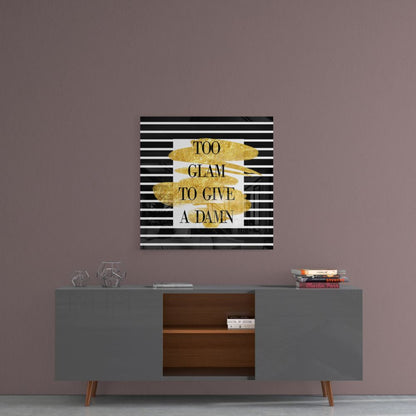 Gold foil and black striped glass wall art displaying "Too Glam to Give a Damn" text mounted above a gray sideboard.