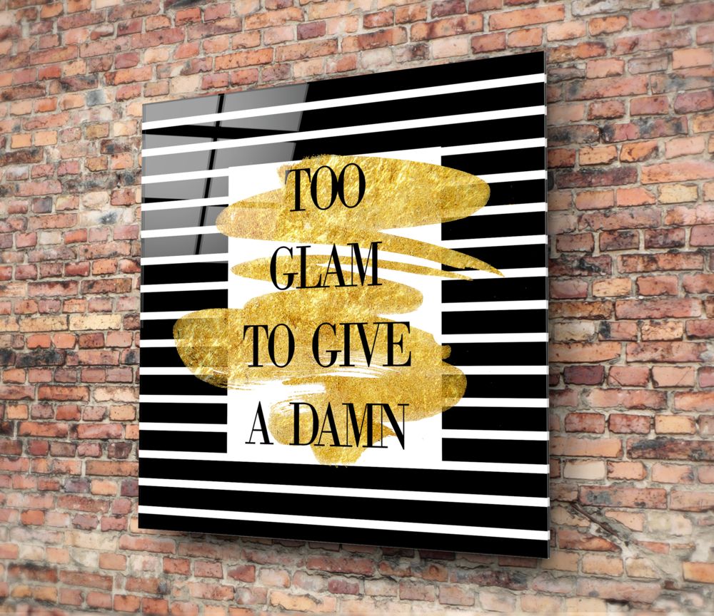 Sparkle glass wall art with black and white striped background and gold leaf accents displaying "TOO GLAM TO GIVE A DAMN" text, mounted on red brick wall.