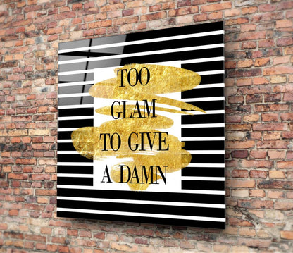 Sparkle glass wall art with black and white striped background and gold leaf accents displaying "TOO GLAM TO GIVE A DAMN" text, mounted on red brick wall.