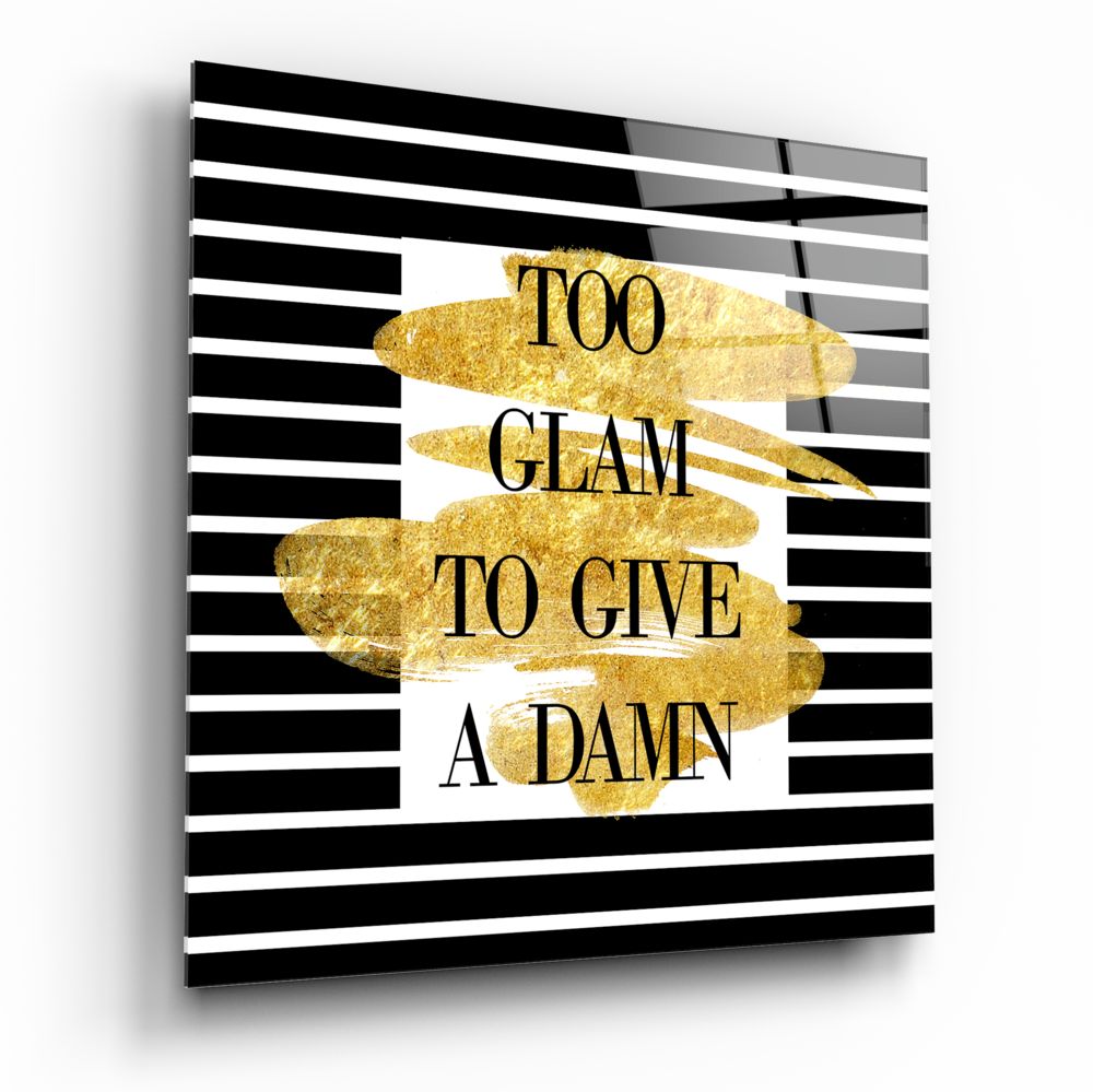 Angled view of glass wall art with black and white horizontal stripes, gold brushstroke shapes, and text reading "TOO GLAM TO GIVE A DAMN.