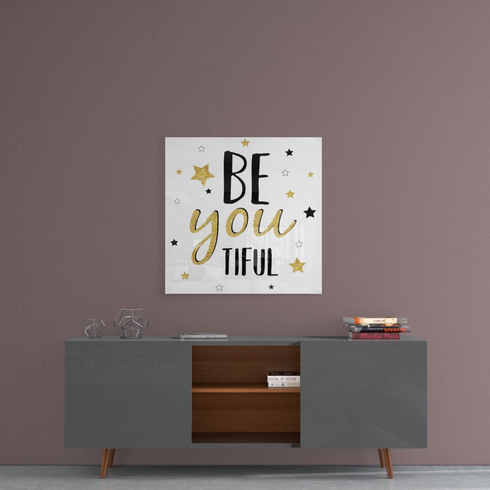 Motivational glass wall art with "BE you TIFUL" text and gold and black stars displayed above a gray mid-century modern credenza against a mauve wall.