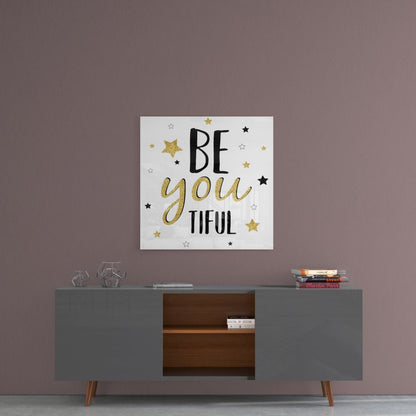 Motivational glass wall art with "BE you TIFUL" text and gold and black stars displayed above a gray mid-century modern credenza against a mauve wall.
