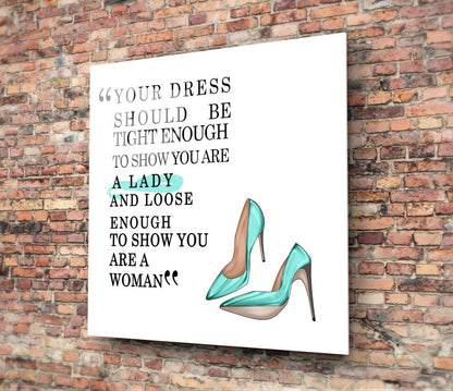 White glass wall art with black and teal text and illustration of turquoise high heels mounted on red brick wall.