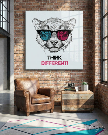 Glass wall art featuring a lion wearing turquoise and magenta sunglasses with "THINK DIFFERENT!" text, displayed in a loft space above a leather chair.