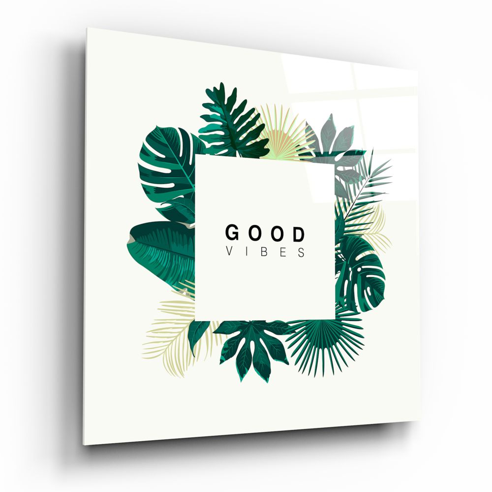 Square glass wall art panel with cream background, green and gold tropical leaf border design, and "GOOD VIBES" text centered, shown at angled perspective.