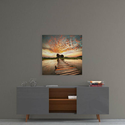 Glass wall art depicting a wooden dock extending into still water at sunset with orange clouds and distant trees.