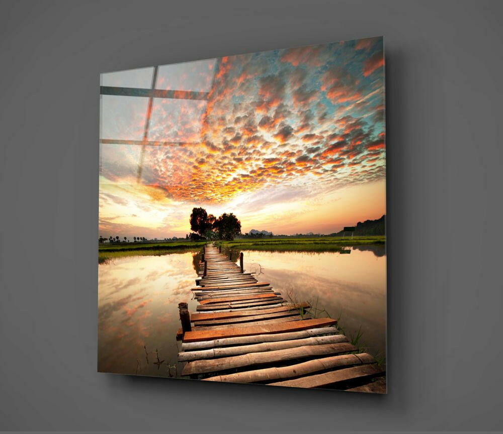 Wooden dock extending into calm water under dramatic sunset sky with orange clouds, displayed as glass wall art with grid overlay.