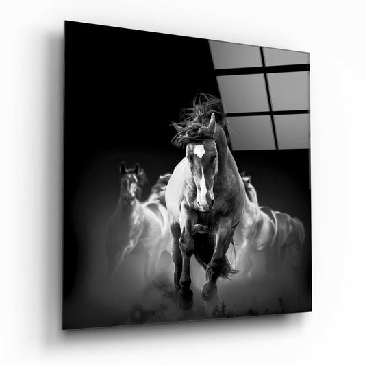 Black and white glass wall art panel displaying a galloping horse with white blaze running toward camera, additional horses blurred in background.
