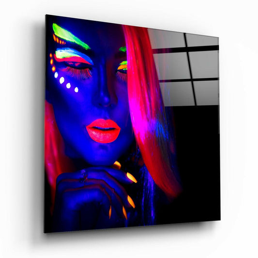 Angled view of glass wall art showing neon-lit female portrait with blue skin, hot pink hair, and fluorescent makeup details against dark background.