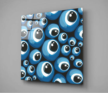 Square glass wall art displaying a densely packed pattern of blue evil eye beads with white rings and black pupils against a black background, mounted at an angle on gray wall.