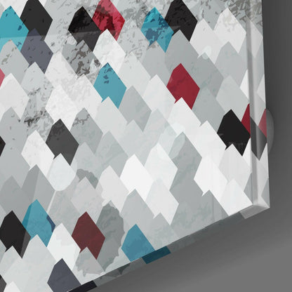 Glass wall art panel displaying a diamond argyle pattern in white, gray, teal, burgundy, and black tiles, photographed at an angle against a gray wall.