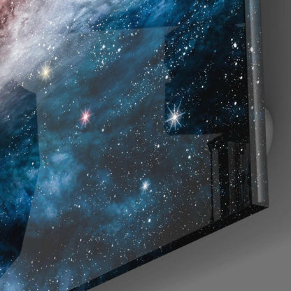 Blue Infinity Glass Wall Art displayed at an angle showing a starfield with bright stars and nebula clouds against gray wall background.