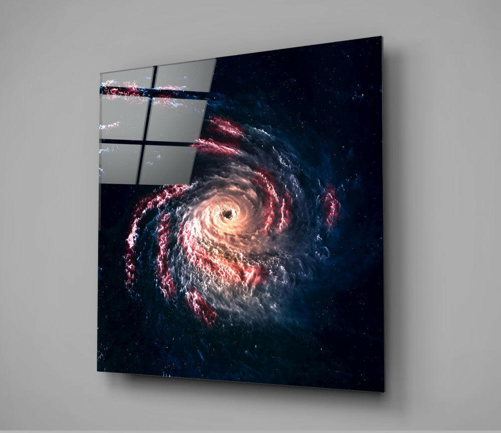Black hole glass wall art mounted on white wall, displaying a spiral galaxy with glowing orange center and red and blue cosmic dust against dark space background.