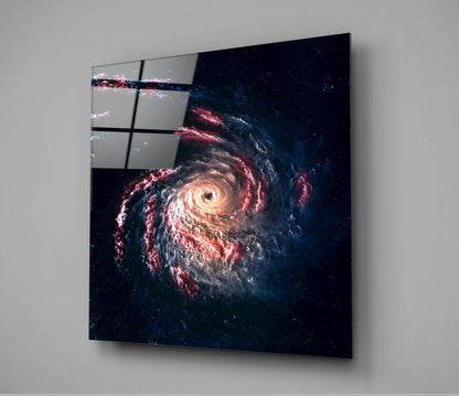 Black hole glass wall art mounted on white wall, displaying a spiral galaxy with glowing orange center and red and blue cosmic dust against dark space background.