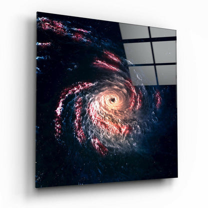 Angled view of square glass wall art depicting a glowing spiral galaxy with red and white clouds against dark space, with gray panels visible in upper right corner.
