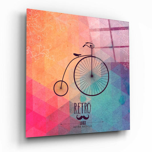 Angled view of glass wall art featuring a penny-farthing bicycle silhouette against a gradient background transitioning from coral and orange to pink, purple, and teal, with ornamental patterns and "RETRO 1882 RETRO BICYCLE" text.