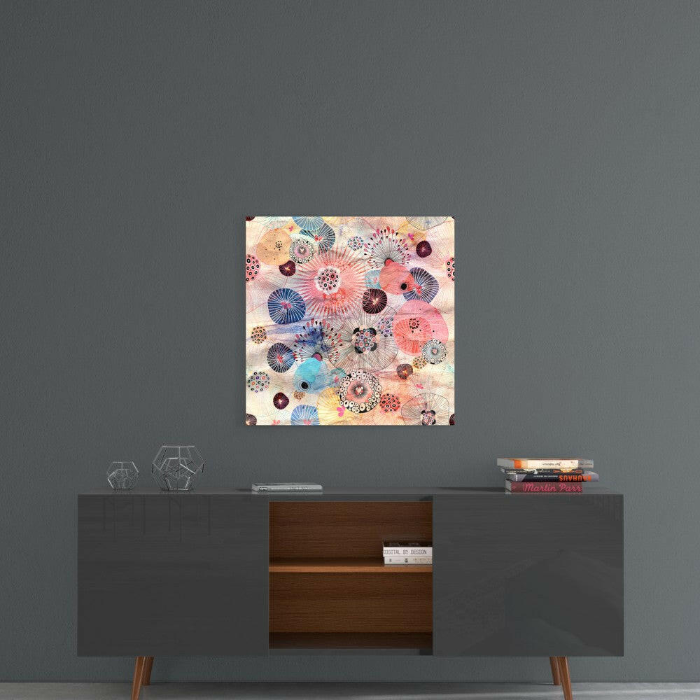 Square glass wall art with colorful geometric flower and mandala patterns in pink, blue, coral, and gold displayed above a mid-century modern sideboard.