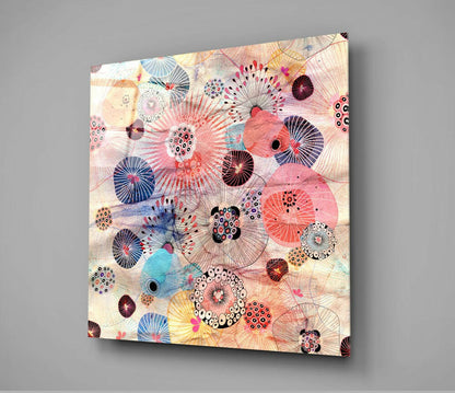 Square glass wall art panel displaying abstract floral design with pink, blue, and cream circles and radiating line patterns against light background.