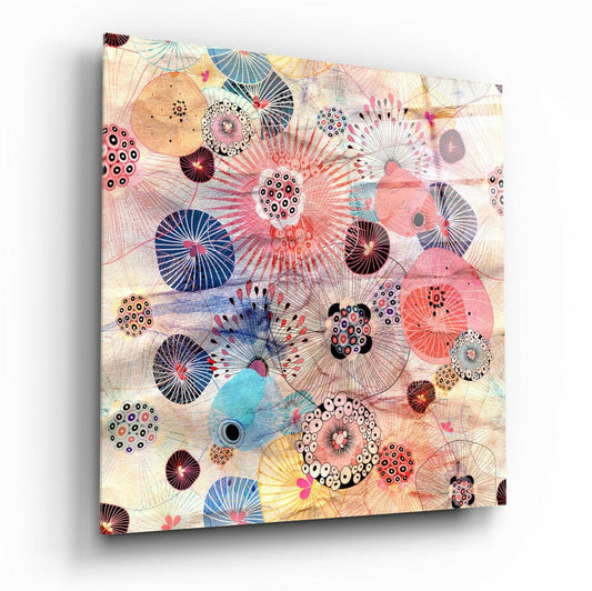 Glass wall art panel displaying intricate floral and circular patterns in pink, blue, yellow, and black on cream background, angled view.