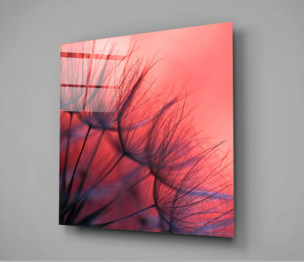 Red dandelion glass wall art displayed at an angle, showing delicate seedhead silhouettes against a gradient coral-to-deep-red background with window blind shadows.