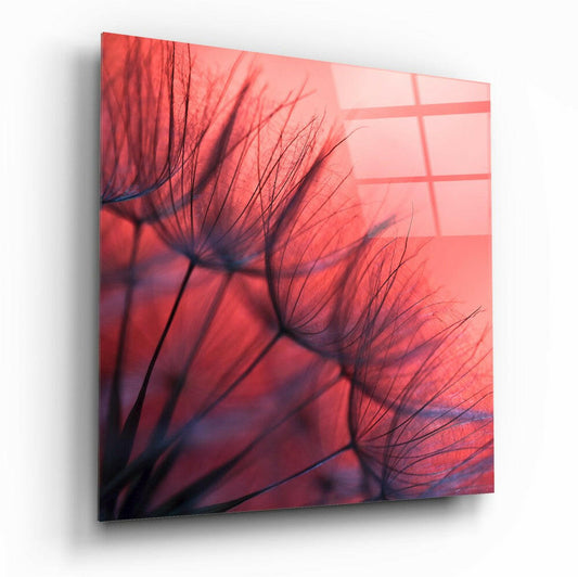 Red dandelion glass wall art displayed at an angled perspective, showing delicate seed heads silhouetted against a coral-red gradient background with window grid shadows.