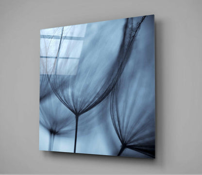 Angled view of glass wall art displaying translucent dandelion seed heads in blue and black tones against light background.